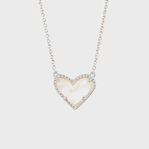 A heart-shaped pendant with a pearly center adorned with small gems rests on a silver chain against a plain white background.