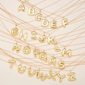 Gold letter pendants hang on thin chains, neatly laid out on a light background, forming the entire alphabet from A to Z.