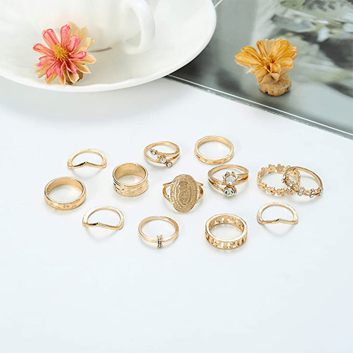 Gold rings lie arranged on a white surface beside a teacup, saucer, and two flowers, one pink and one yellow.