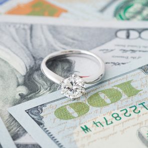 A diamond ring rests on a stack of hundred-dollar bills, showcasing wealth and luxury.