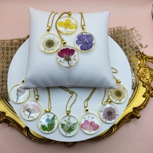 Necklaces display pressed flowers enclosed in circular pendants, arranged on a white pillow atop a decorative golden tray with burlap accent.