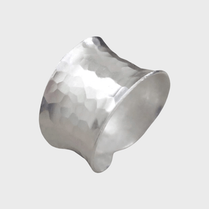 Silver ring exhibits a hammered texture, featuring a wide band shape, against a plain, light gray background.