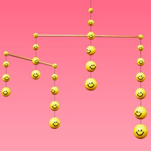Yellow smiley face balls hang from strings, creating a mobile, against a pink gradient background.