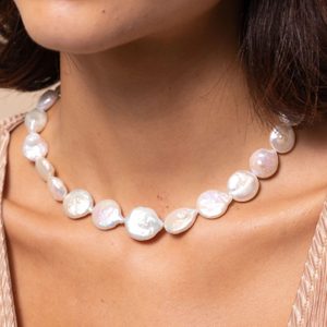 Pearl necklace rests on a woman's neck, with uneven pearls reflecting soft light in a neutral setting.