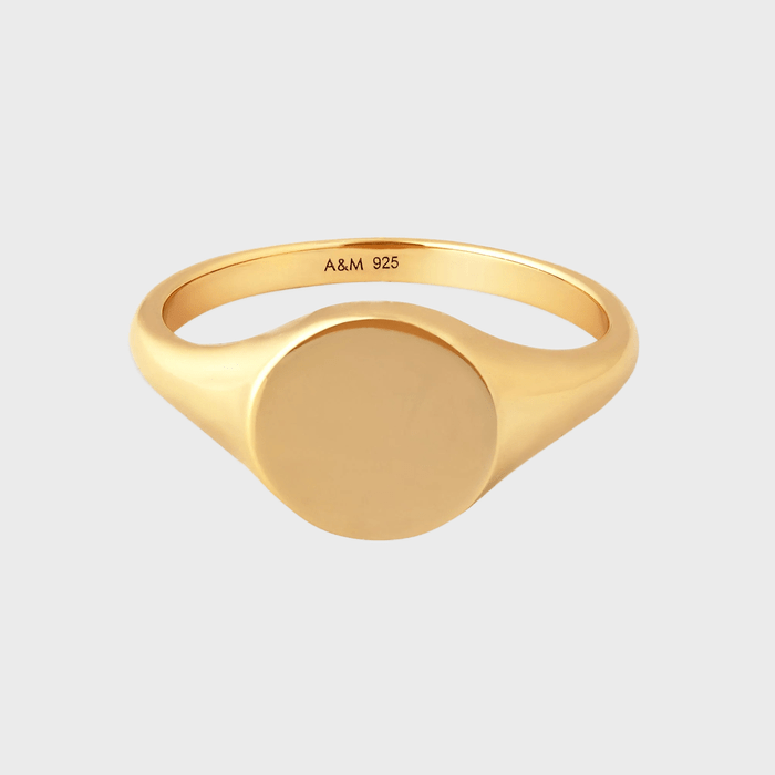 Gold signet ring rests against a plain background, inscribed with 