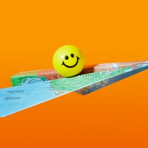 Smiley face ball rests on a paper airplane made from a world map against an orange background.