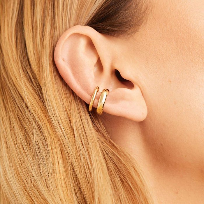 Gold hoop earrings adorn an ear, surrounded by light brown hair, enhancing an elegant and simple style.