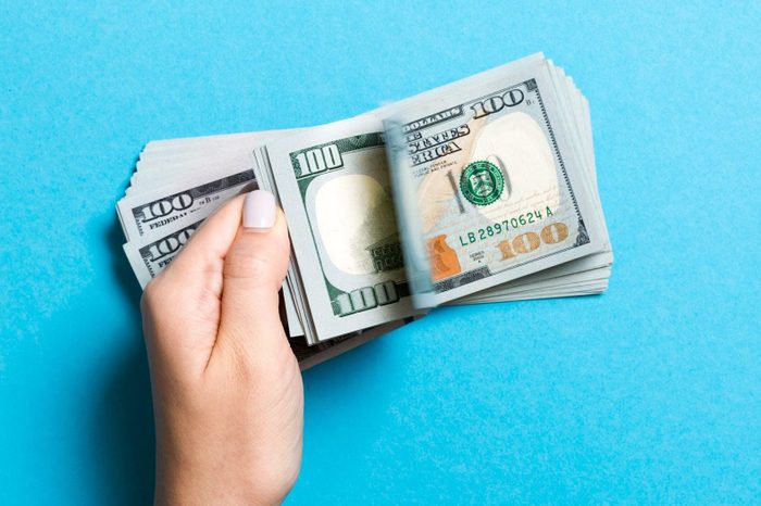 Close-Up Of Hand Holding Paper Currency Against Blue Background
