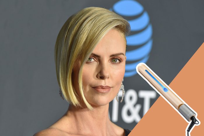 Person gazes forward, featuring short blonde hair and earrings, against a backdrop with blue logo. Nearby, a golden hair styling tool is angled.