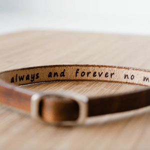 Leather bracelet lying flat, with engraved text reading 