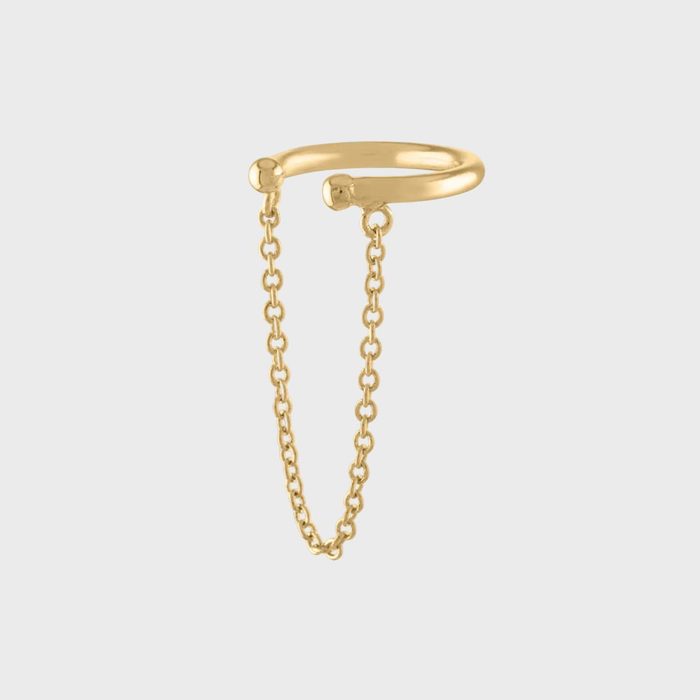 Gold ring dangles thin chain, suspended against a plain gray background.