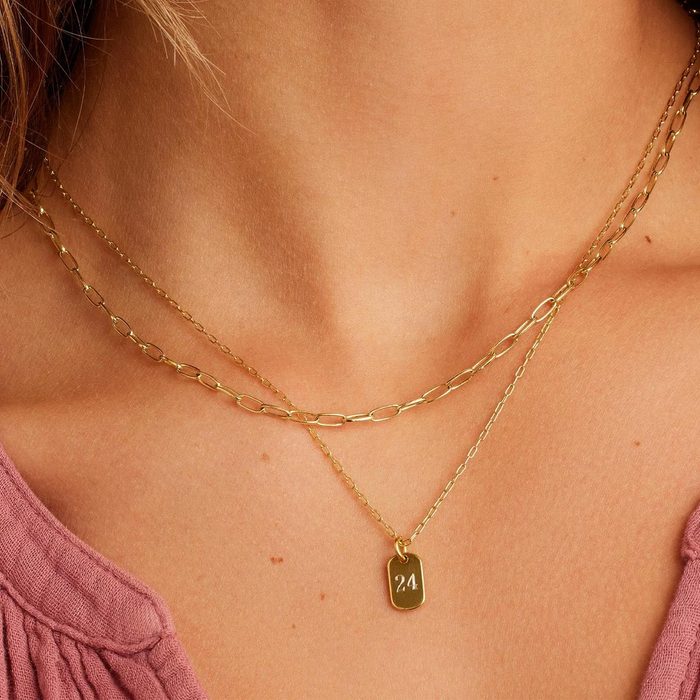 Gold necklaces rest on a person's neck, featuring a pendant with 