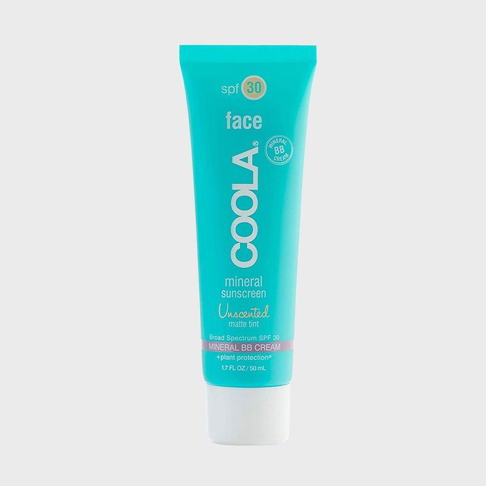 A turquoise tube displays sunscreen, standing upright in a light gray setting. It reads: 