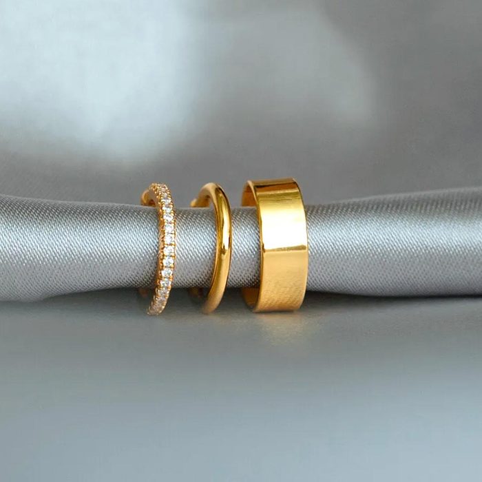 Three gold rings rest on a gray satin cloth; one has diamonds, the others are plain and smooth.