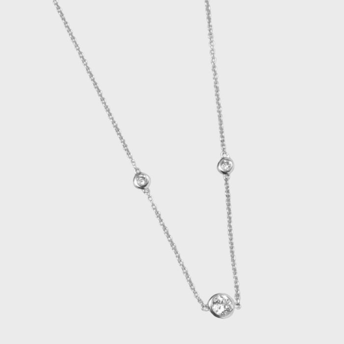 Necklace features spaced round diamond-like stones on a delicate silver chain, set against a plain white background.