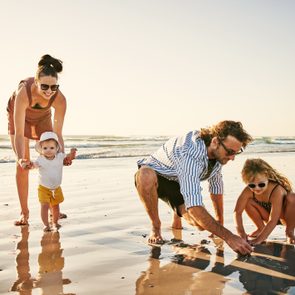 Family explores wet sand together on a sunny beach.