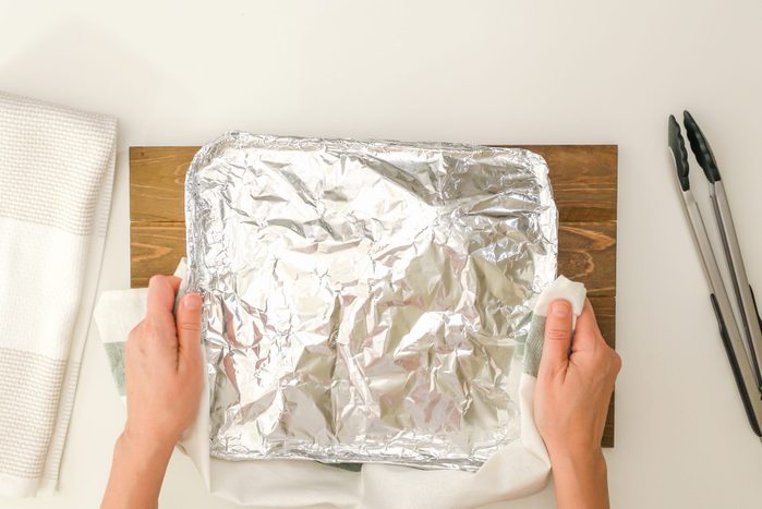 Chef taking off aluminum foil. Spicy marinated turkey legs cooked in a disposable bake-ware pan, just from the oven, close up view from above. Step by step roasted turkey recipe