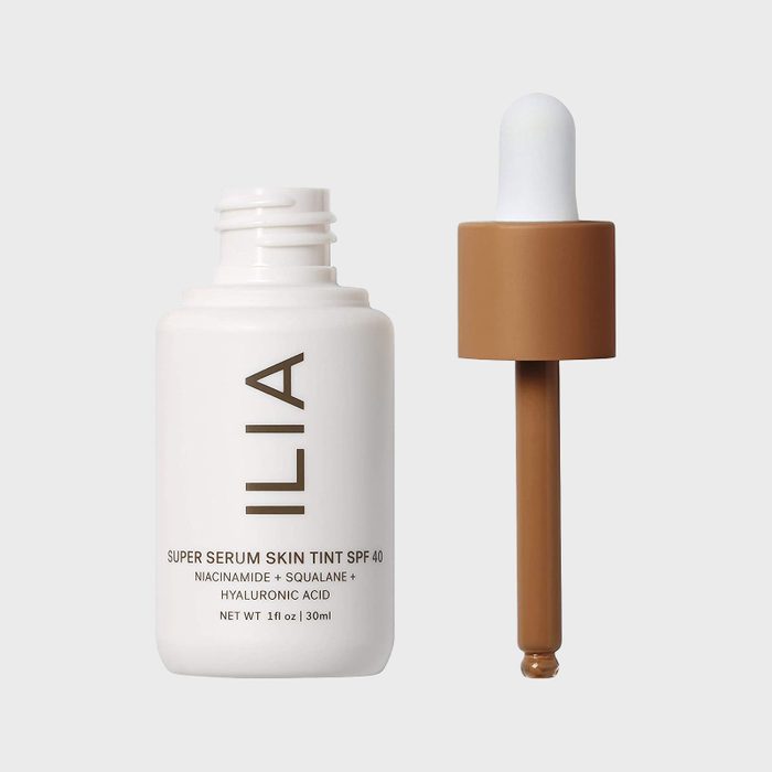 A dropper dispenses a liquid. The bottle reads: ILIA Super Serum Skin Tint SPF 40, Niacinamide, Squalane, Hyaluronic Acid, Net wt 1 fl oz.