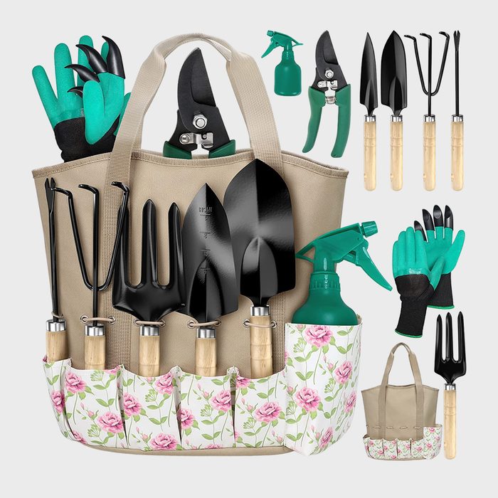 Garden tools arranged in a beige tote with floral pockets, including trowels, pruning shears, and gloves. A green spray bottle is also present.