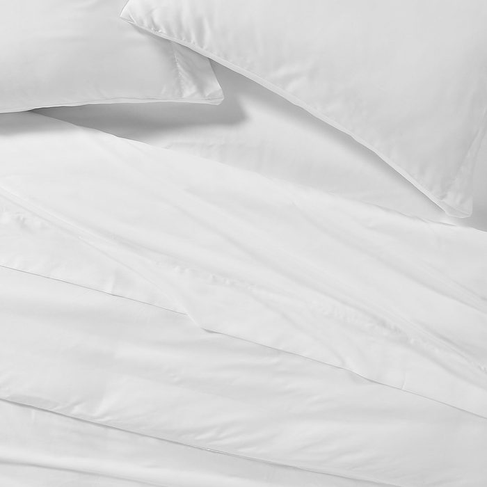 White pillows and sheets lie flat on a bed, creating a crisp, clean appearance in a simple bedroom setting.