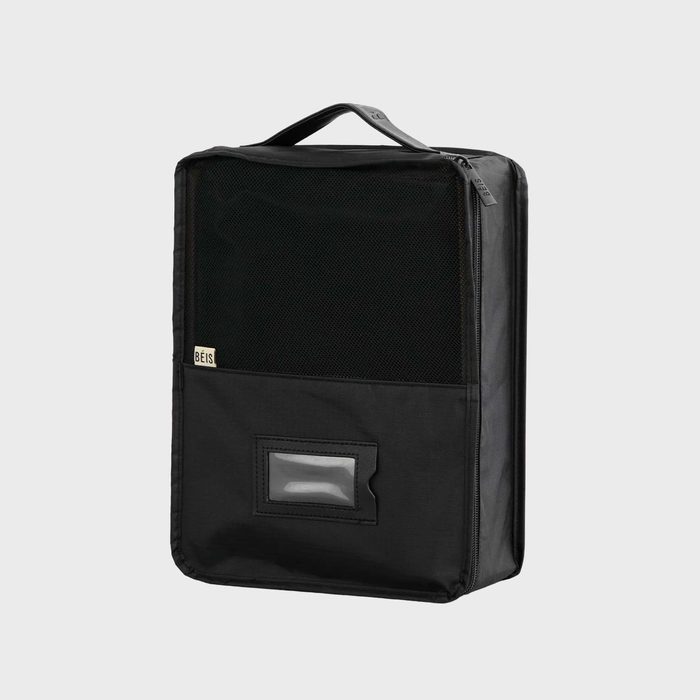 Black travel case stands upright, featuring a handle, zippered closure, and mesh front pocket with a transparent ID slot, in a neutral studio setting.
