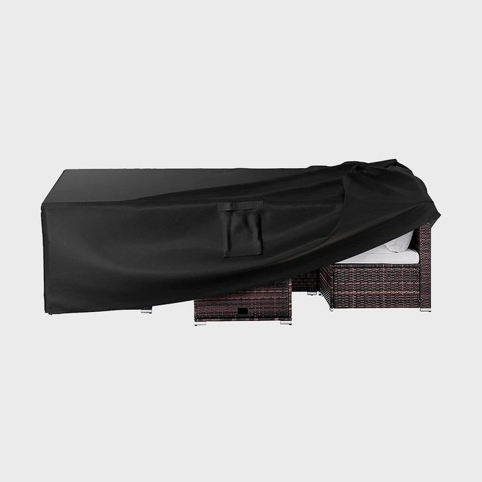 Black cover partially reveals wicker furniture with cushions in a simple, neutral indoor or outdoor setting.