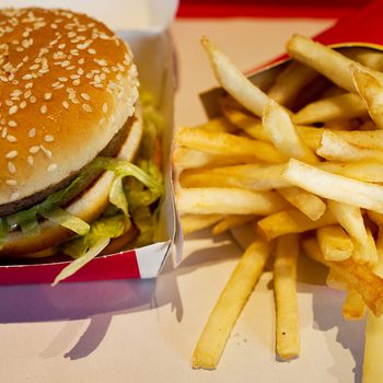 A sesame seed hamburger rests in an open box beside a container of golden fries on a fast-food tray.