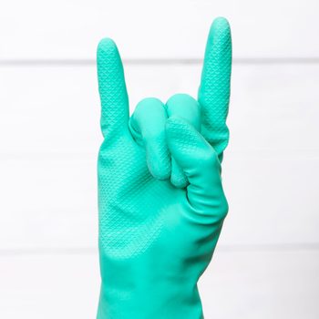 A green rubber-gloved hand forms a "rock on" gesture against a plain white background.