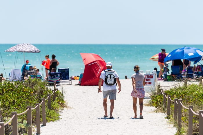 couple walking on sandy trail path walkway by fence to Bowman's beach, Sanibel Island, Florida, USA, with other beachgoers in the background