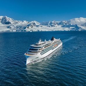Cruise ship sails across blue ocean, surrounded by snow-covered mountains and icebergs under clear sky.