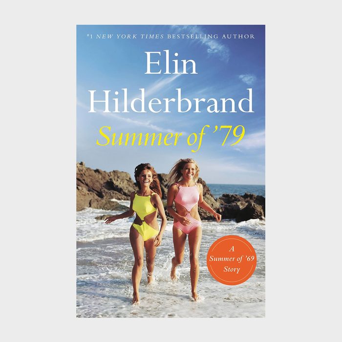 Two women run on a beach, smiling, wearing swimsuits. Background includes rocky shore and ocean. Text reads 