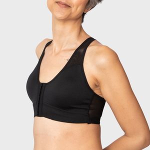 A person wears a black front-closure sports bra, standing against a plain, light gray background.