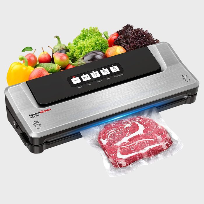 Vacuum sealer sealing steak in a bag; surrounded by fresh vegetables. Features control buttons on the top panel.