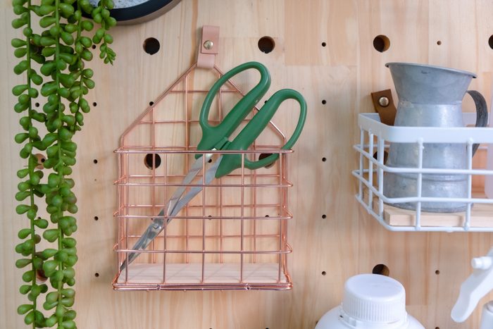 Green scissors in pink gold basket metal hanging on a Pine wood pegboard.