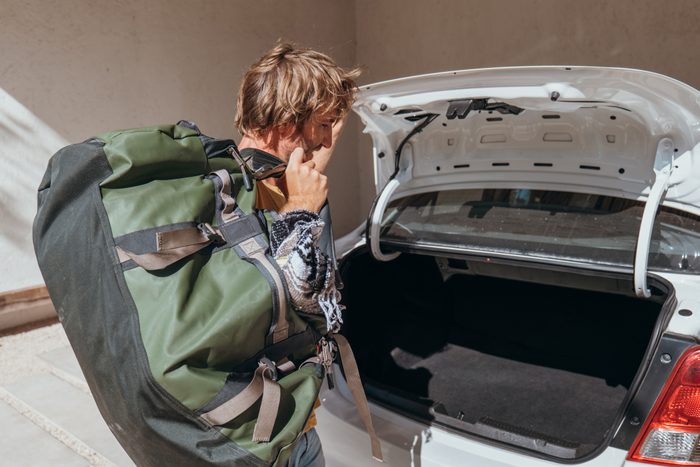 Male packing for a trip loading his baggage onto a car trunk