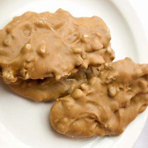 Three pralines rest on a white plate, their nutty texture visible, set against a plain background.