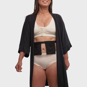 Woman wearing a beige bra and underwear set with a black robe, standing against a plain background, smiling slightly.
