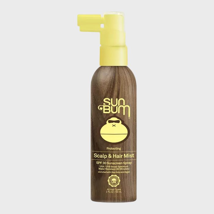 Bottle sprays sunscreen mist, featuring yellow nozzle and logo on a wood-patterned backdrop, labeled 