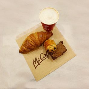 Croissant, mini pastry, and brownie rest on a McCafÃ© napkin. Nearby, a red cup of coffee sits on a marble surface.