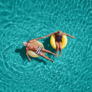 Two people float on inflatables, holding hands in a clear blue pool, creating ripples around them.
