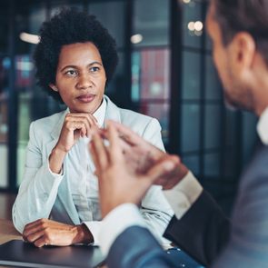 Woman attentively listens to a man speaking across a table in a modern office setting.