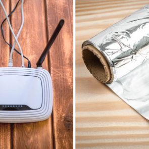 Router sits on wooden surface with cables attached; aluminum foil roll lies partially unrolled on patterned wooden table.