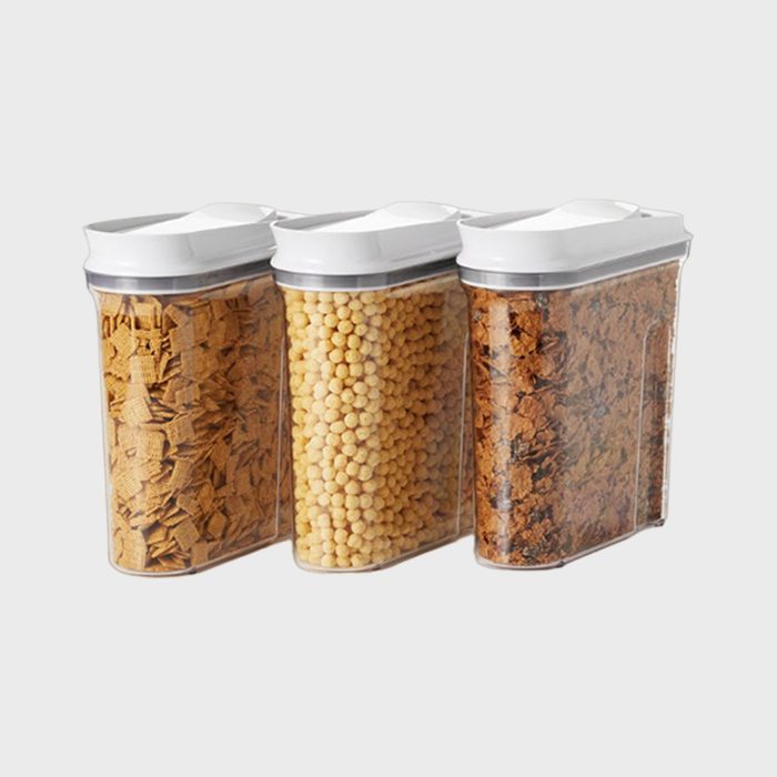Three transparent containers hold different cereals with white lids, arranged side by side against a plain gray background.