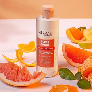 Shampoo bottle stands among sliced citrus fruits and leaves on a light surface.