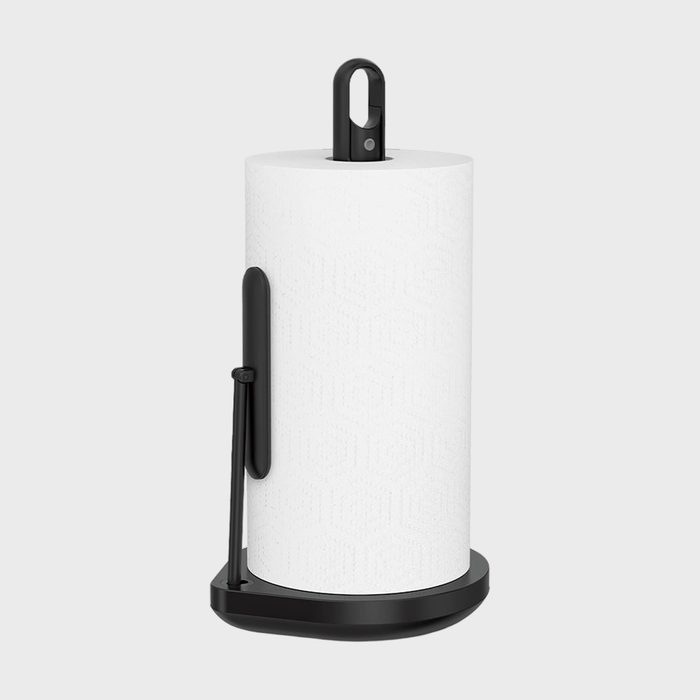 A paper towel roll stands vertically on a black holder with a handle in a plain, light-gray background.