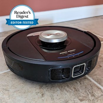 Robot vacuum on tiled floor, cleaning near a wall, with "Reader's Digest Editor-Tested" badge beside it.