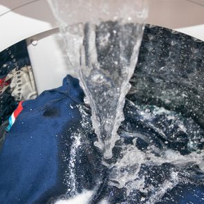 Water flows onto blue clothes inside a washing machine, with soap suds visible around the fabric in a metallic drum.