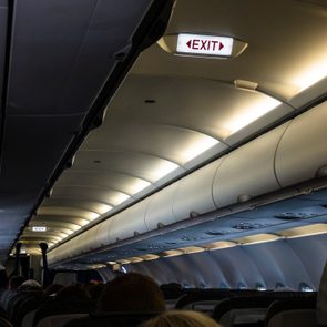 Airplane cabin interior; passengers seated beneath illuminated 