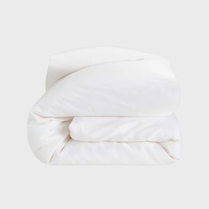 A neatly folded white duvet lies against a plain gray background, showing smooth fabric and soft contours.