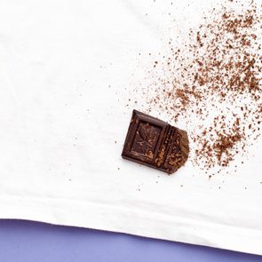 Chocolate piece lays partially eaten, leaving crumbs scattered on a white cloth against a purple surface.